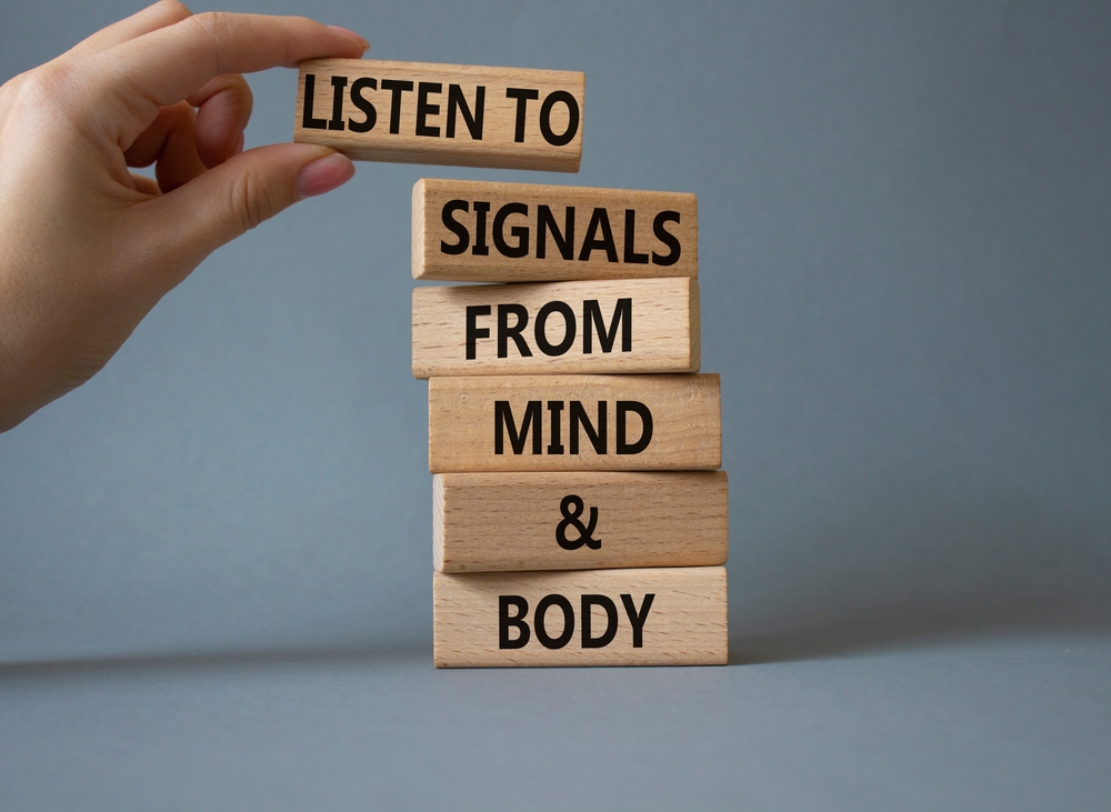 Body and mind wellness symbol. Concept words Listen to signals from mind and body on wooden blocks. Beautiful grey background. Doctor hand.