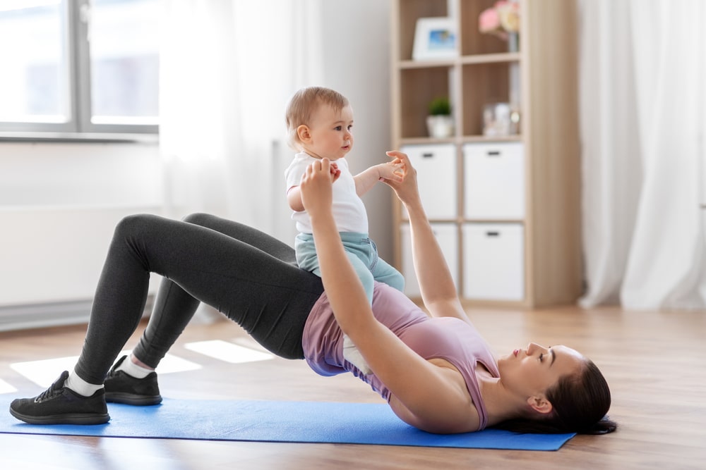 Mother with little baby exercising at home.