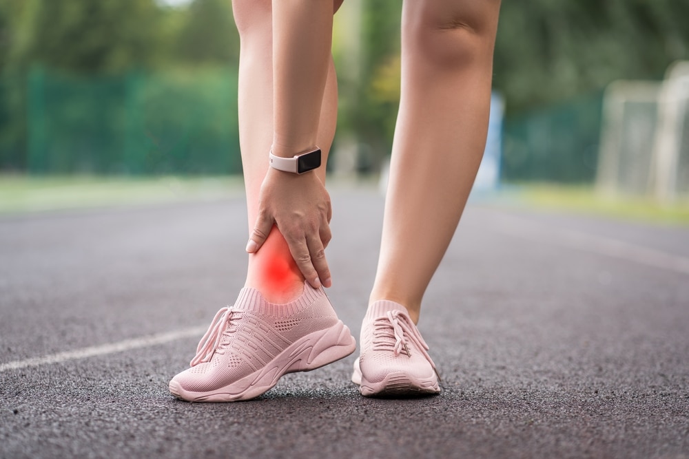 Achilles tendon injury, callus on the heel while running, foot pain, woman suffering from feet ache on a sports ground, podiatry concept.