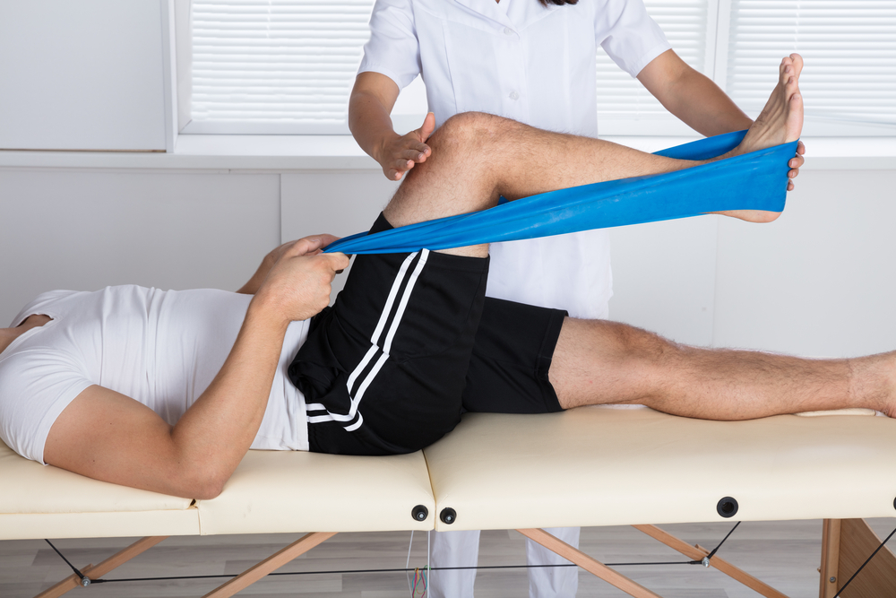 A physical therapist helps a man with knee pain by performing a leg stretch, aiming to improve his range of motion and comfort.